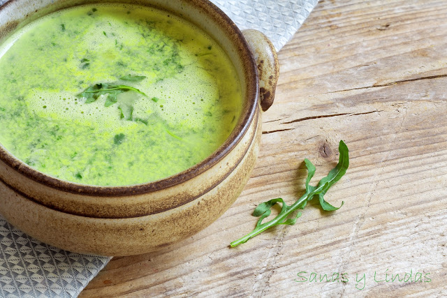 cazuela con sopa crema verde y una hojita de rúcula sobre mesa de madera