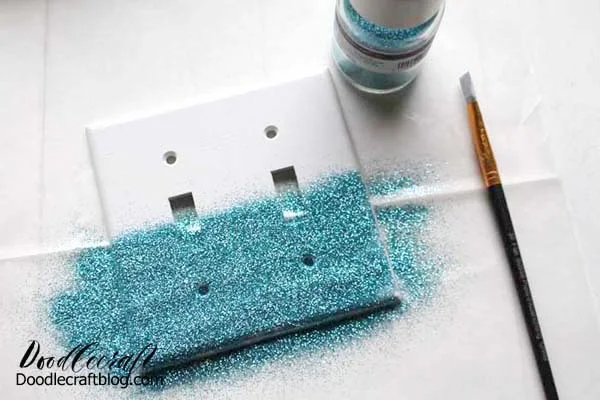 I used aqua glitter, my favorite color.  Then gently lift up the switch plate to dump all the excess glitter off onto the work surface.   Lift the paper and pour the glitter back into the jar.