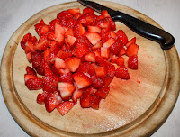 A wooden chopping board full of finely chopped strawberries