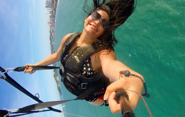 mulher com um paraquedas e sentada em uma cadeirinha puxada por uma lancha no mar