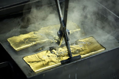 freshly minted gold bars being extracted from a water bath