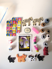 Selection of miniature items laid out on a tabletop, including woven vases, tissue holders, posters and plastic flamingos.
