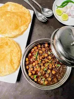 Serving two bhature with chole and onion slices, lemon wedges,green chili, spoon and fork in background