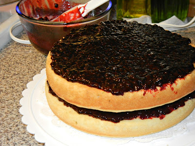 2 layer cake with blackberry jam in the middle and on top on a white cake stand 