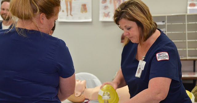 Woman in nursing attire performs a checkup on a mannequin