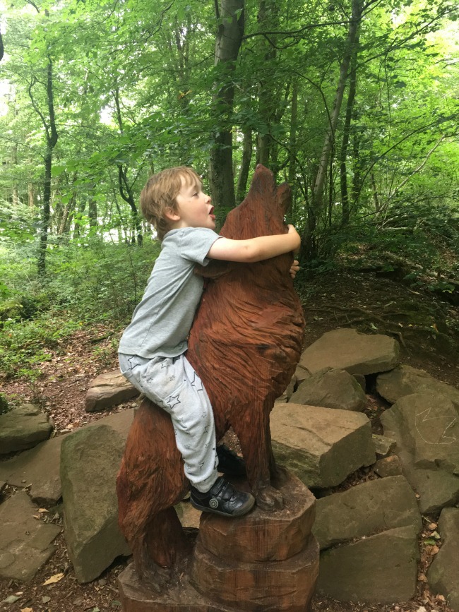 image-of-boy-sitting-on-wolf-sculpture-and-both-howling-at-Fforest-fawr