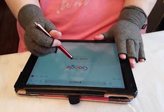 A woman's hands wearing gray fingerless compression glove, holding a stylus pen, using an electronic tablet.