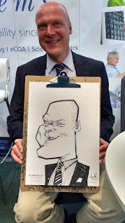 Caricatura de señor calvo, en traje y de edad mediana posando con su caricatura hecha en vivo.