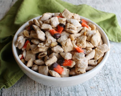 Puppy chow or muddy buddies are perfect little sweet treats for any occasion. They are generally super fast and easy to make and so much fun to eat. This collection of great recipes is sure to inspire you whip up several batches! serving bowl filled with peanut butter white chocolate and candy corn squirrel puppy chow