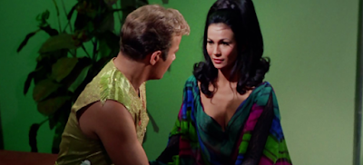 Kirk talking to a curly-haired brunette wearing a bathrobe with dark blue, green, and purple patterns