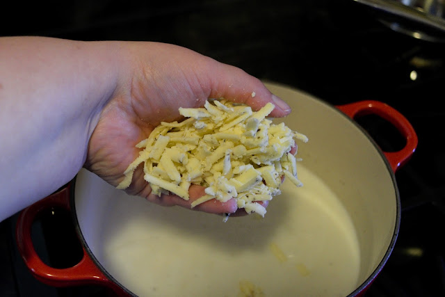The shredded, truffled cheddar cheese being added to the white sauce.