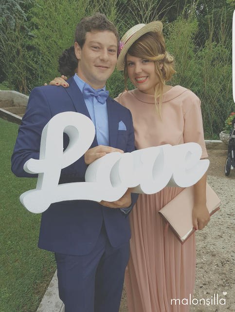 Pareja de invitados de boda posando con cartel de letras love en blanco