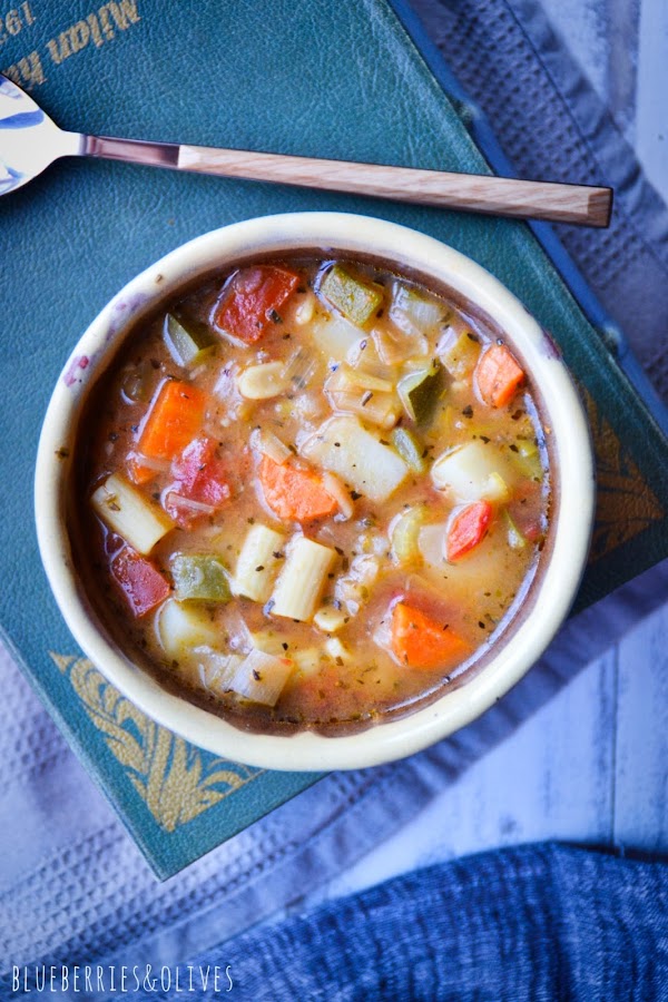 bol cerámica con sopa SOBRE LIBRO ANTIGUO, paño lino gris, libro cocina del mundo, cuchara mango madera,hojas perejil fresco