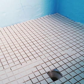 Shower floor with new small square white tiles and walls covered with blue waterproofing membrane.