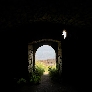 Looking out from the Monk’s Cave - a photo from inside the cave looking out through the darkness of the building to the doorway and the sea and sky out beyond.  Photo by Kevin Nosferatu for the Skulferatu Project.