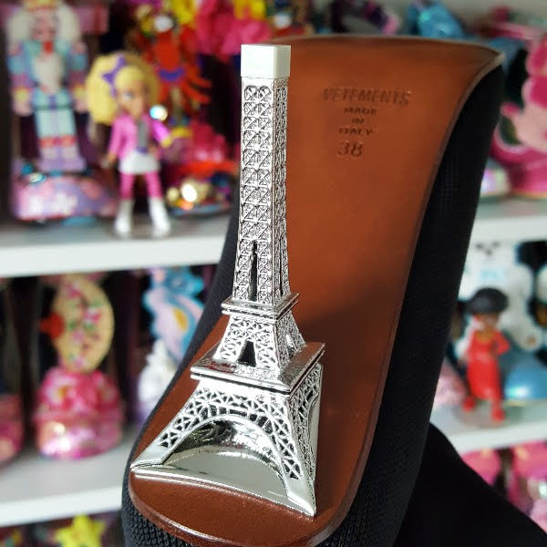 close up of silver metal Eiffel Tower heel on boot with shoe shelves in background