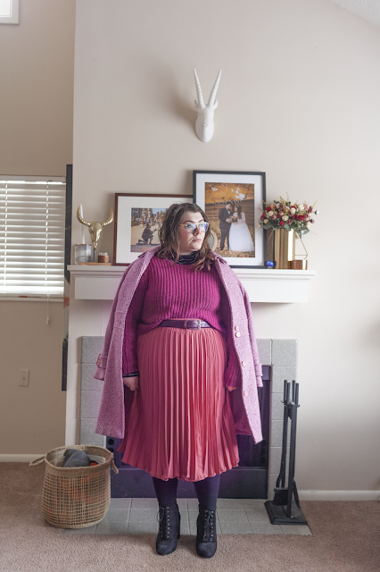 An outfit consisting of a pink marled coat over a berry sweater half tucked into a rose colored pleated midi skirt and black ankle boots.