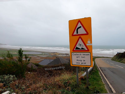 Foto mais ampla da praia com placa de aviso da pista íngreme no País de Gales