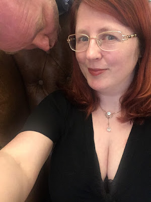 A red-haired woman in a low-cut black dress, and a man staring down her cleavage