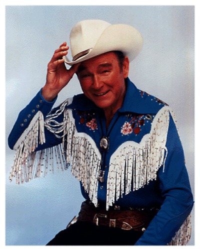 Studio portrait of Roy Rogers in fringed cowboy shirt tipping his white hat