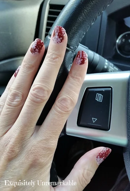 Red Floral Jamberry Nail Wraps on hand on steering wheel.