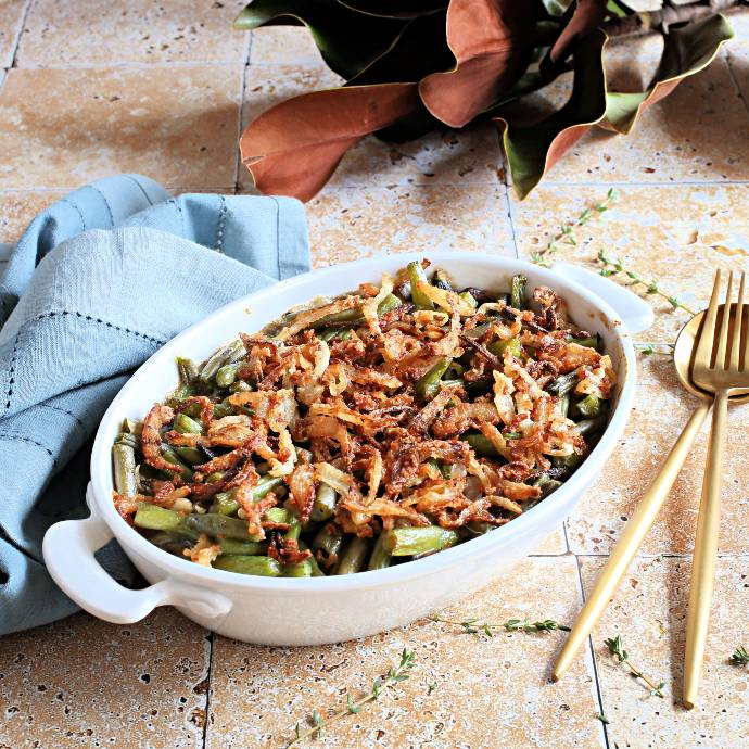 Recipe for a green bean casserole made with mushrooms, caramelized onions and a creamy béchamel sauce, topped with homemade crispy onions.