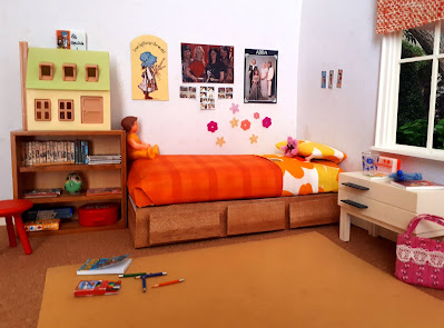 One twelfth scale modern miniature 1970s child's bedroom with a wooden divan bed dressed with bright flowery linen and an orange checked blanket, a bookshelf full of books and a colouring pad and crayons on the rug
