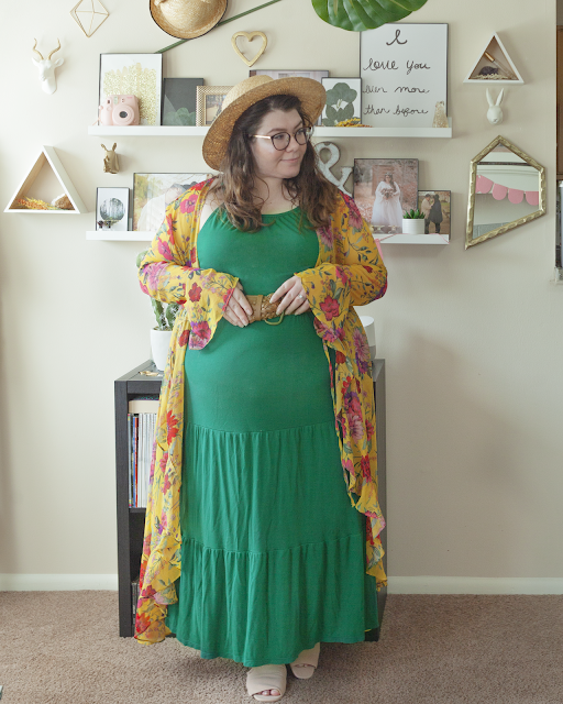 An outfit consisting of a straw boater hat, a long sleeve semi sheer floor length yellow robe with ruffle trim over an olive green sleeveless maxi dress and pink slide sandals.