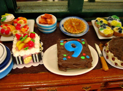 One twelfth scale modern miniature scene of a table laden with cakes and pastries. The cake in the foreground has a number 9 on it.