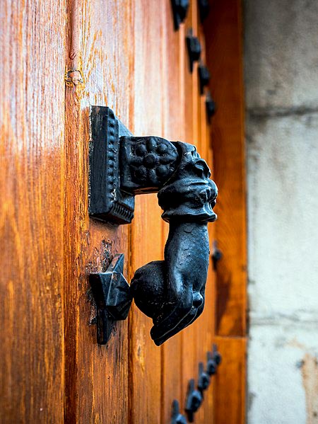 door knocker in the shape of a hand holding a ball, hanging on a rough wooden door