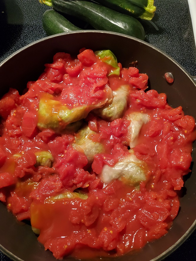 this is cabbage stuffed with meat and rice then with chopped tomatoes on it in a big sauce pot. There is zucchini in the background ready to also stuff