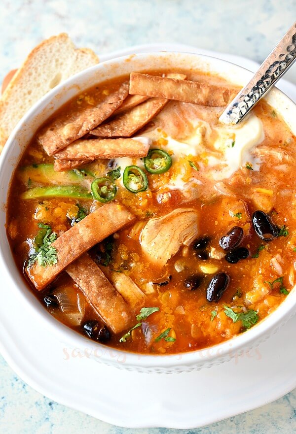 a close up of a white bowl avocado slices,shredded cheese,tortilla chips,sour cream with chicken enchilada soup