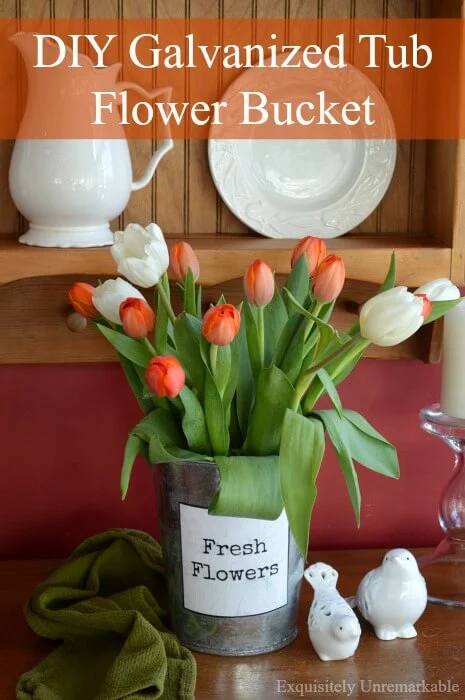 Orange tulips in metal flower vase with printable flowers label on front, sitting on wooden table next to green towel