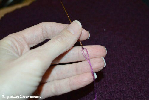 Hand holding a small spool of purple thread