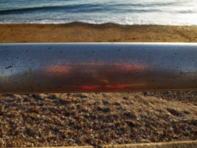 Handrail with pebbles below, sand above and sea beyond