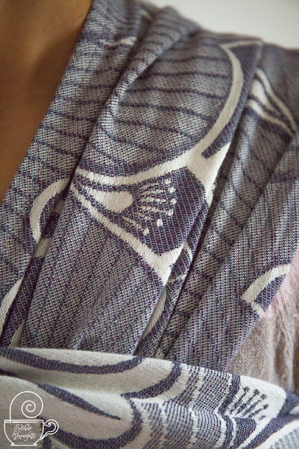 [Image is close-up of a purplish-gray geofloral patterened woven wrap carrier. The different threads and part of the design are apparent.]