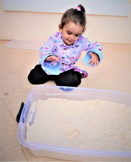 Little girl wears foam shoes on her hands to make a deer print in the sand.