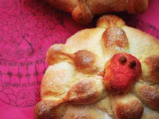Pan de Muerto (Bread of the Dead) A closeup of a Pan de Muerto (Bread of the Dead) roll. It is decorated with a red skull on top and sits on a pink cloth.
