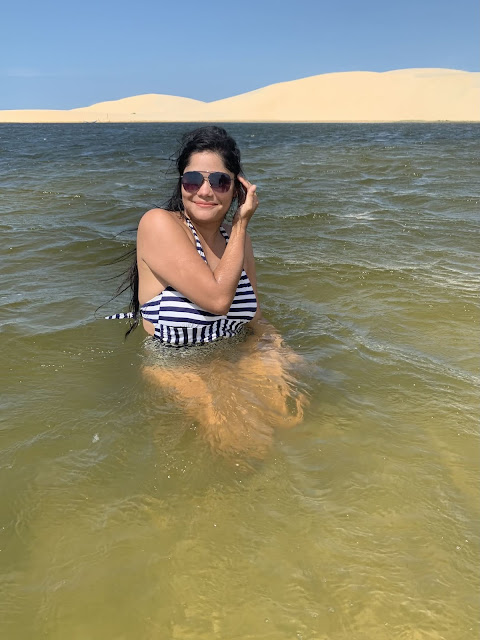 Passeio Quadriciclo em Parnaíba mulher morena, jovem, cabelo preto, oculos escuros, blusa rosa e blaser branco em uma lagoa azul e verde