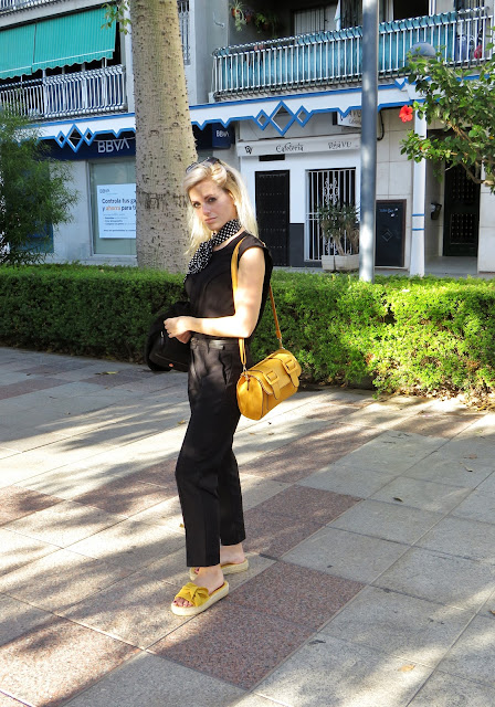 Alejandra Colomera con camiseta negra, pantalón formal negro, lazo en el cuello negro con lunares blancos y complementos mostaza