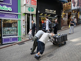 two men pushing containers on a cart up a hill in Hong Kong