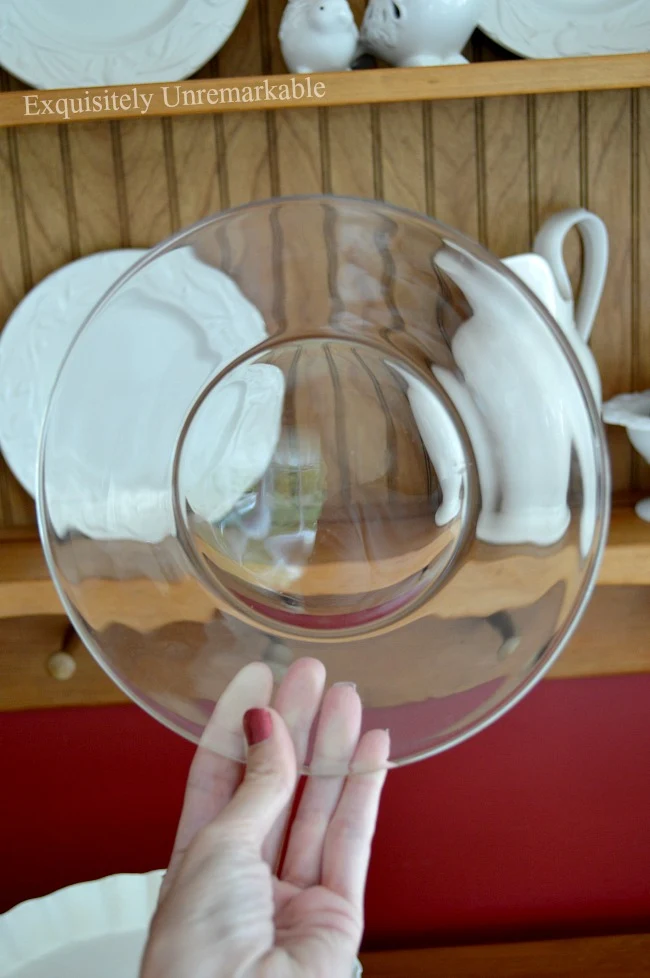 Hand holding up a Dollar Tree glass plate in front of a plate rack