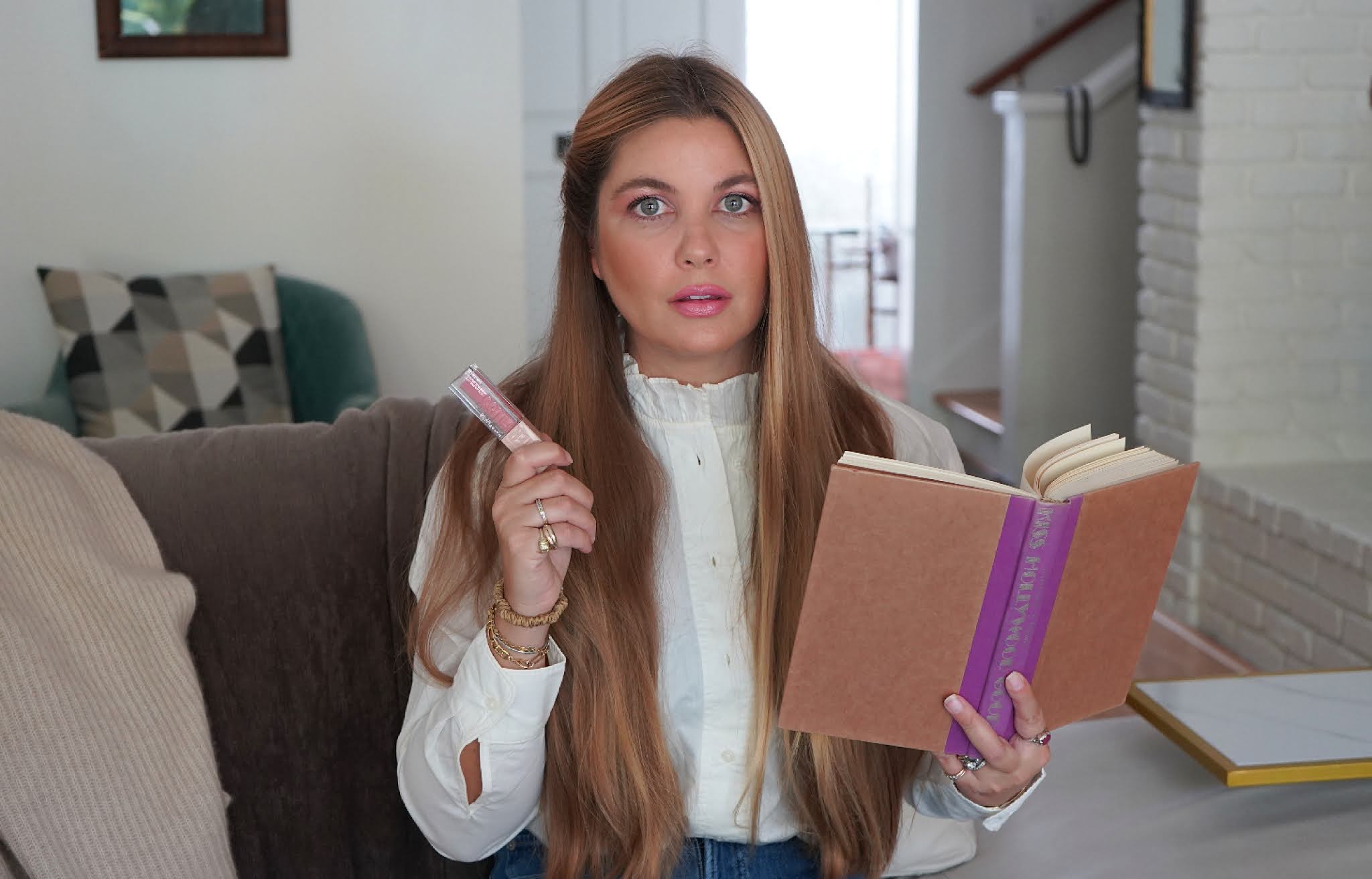 woman reading a book and holding a pink lipstick 