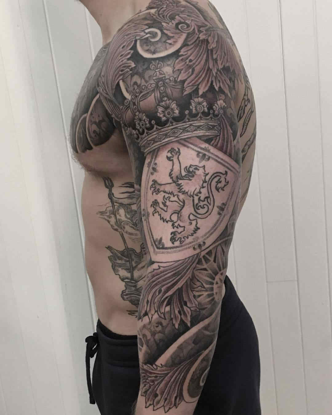 Tatuaje escocés con escudos y emblemas floreados en el brazo de un forzudo