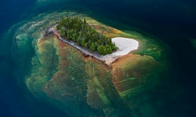 The base of an island fans out beneath the surface of lake superior in 