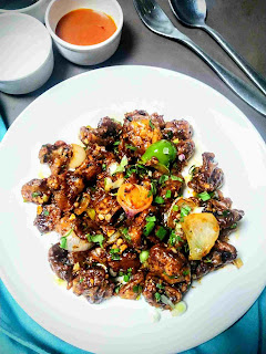 Serving chilli mushroom in a plate, red chilly sauce, fork, spoon in background