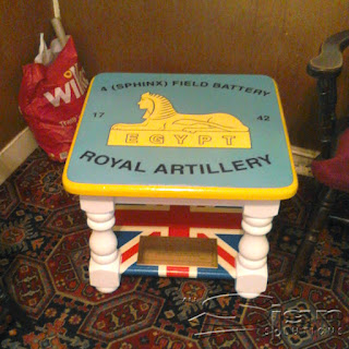 Side table with a blue background, yellow and black writing. The text ontop of the sphinx says "4 Sphinx field battery" and underneath "Royal artillery". The sphinx is sitting on a block with the word 'EGYPT' gerber printed sticker.