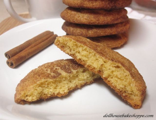 snickerdoodle cookies stacked on a white plate with cinnamon sticks and one cookie broken open to reveal the inside