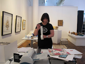 Woman in a gallery during install, pulling book tape of a roll  in the middle of the gallery.