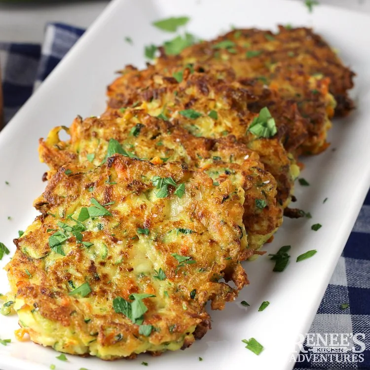 Crispy Zucchini Carrot Fritters on a white platter, ready to eat.